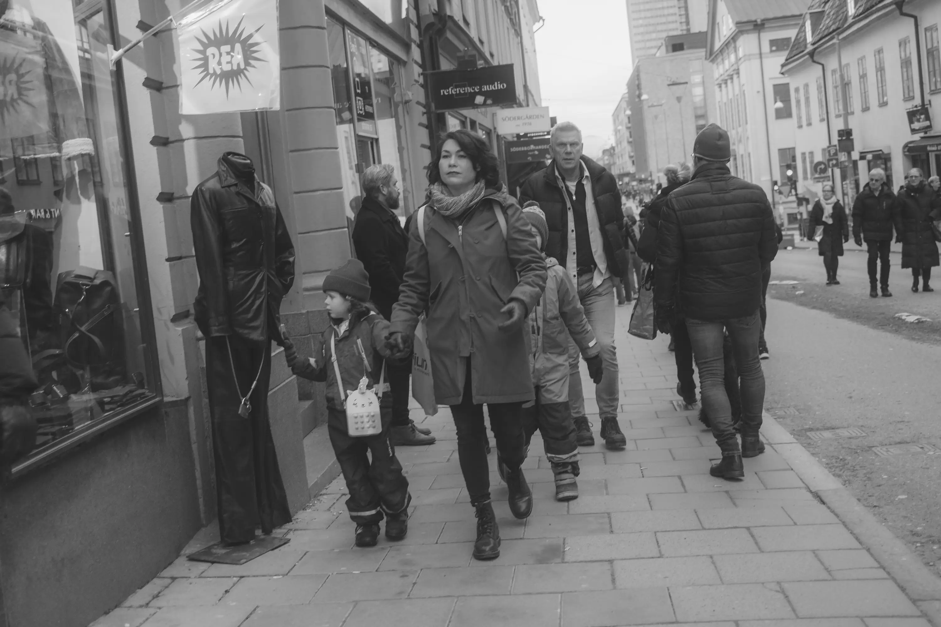 A little girl looking at the price of a coat, dragged by her mother